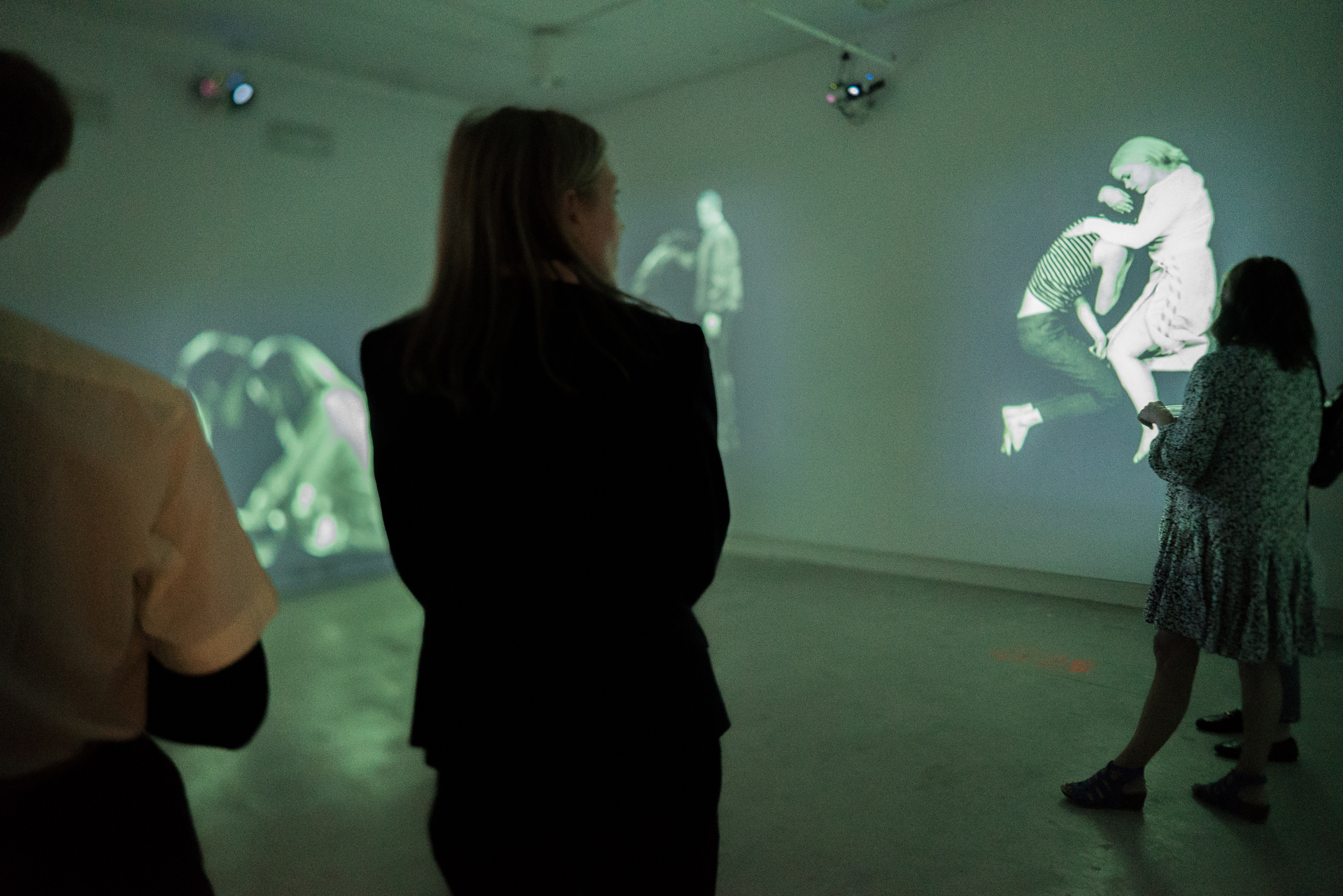 Three people with their backs to the camera viewing a video installation in a gallery.