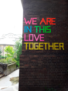 A brick building with the words "We are in this love together" written on it colourful duct tape.