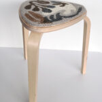 Side view of triangular rug with abstract brown shaded shapes on a wood stool.
