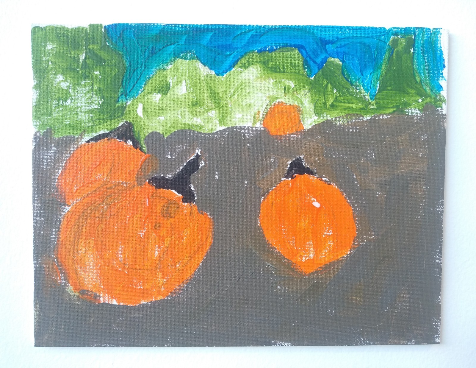 Three pumpkins in an orchard with green trees in the back.