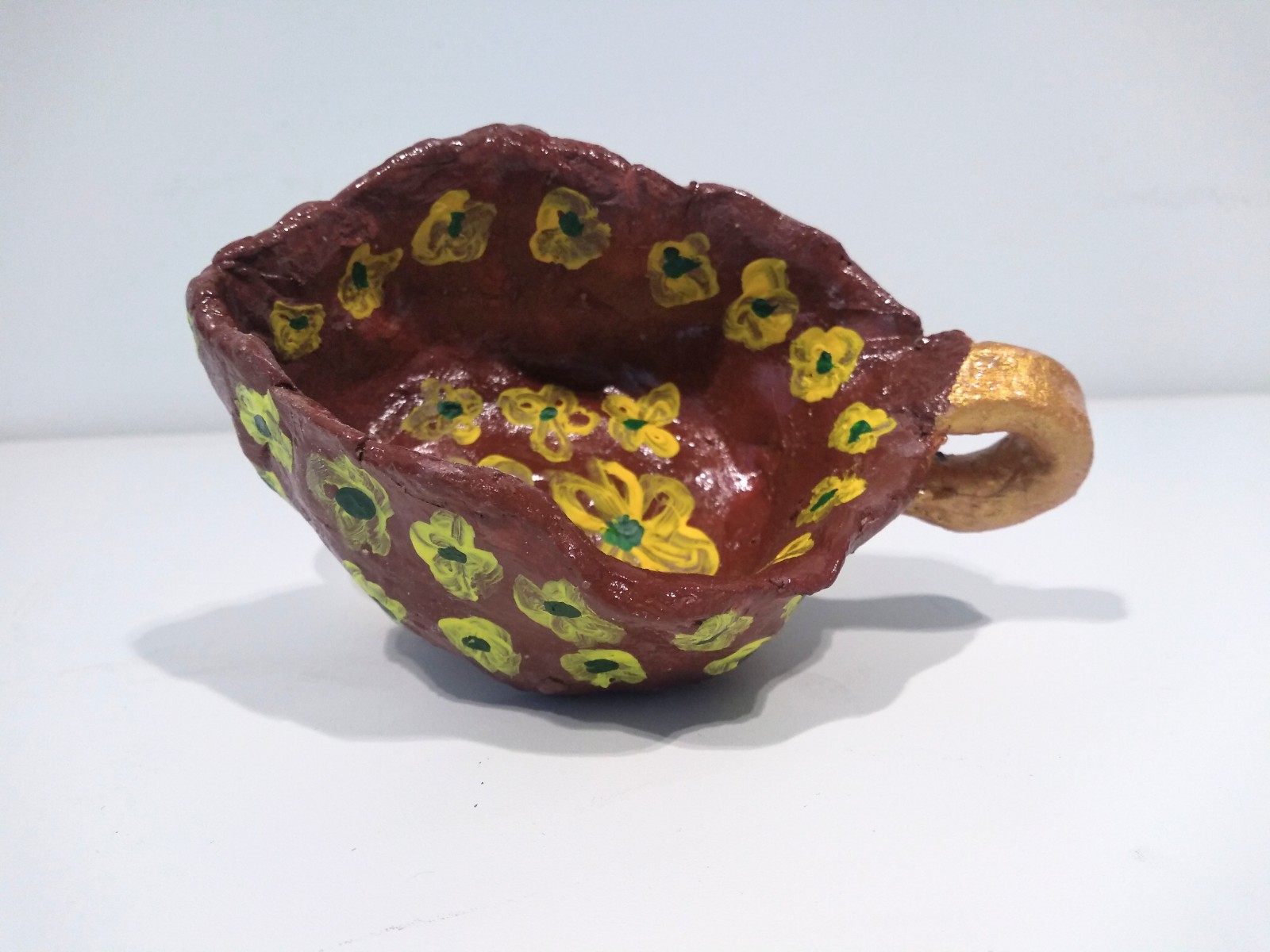 Maroon clay pot with yellow flowers and gold handle.