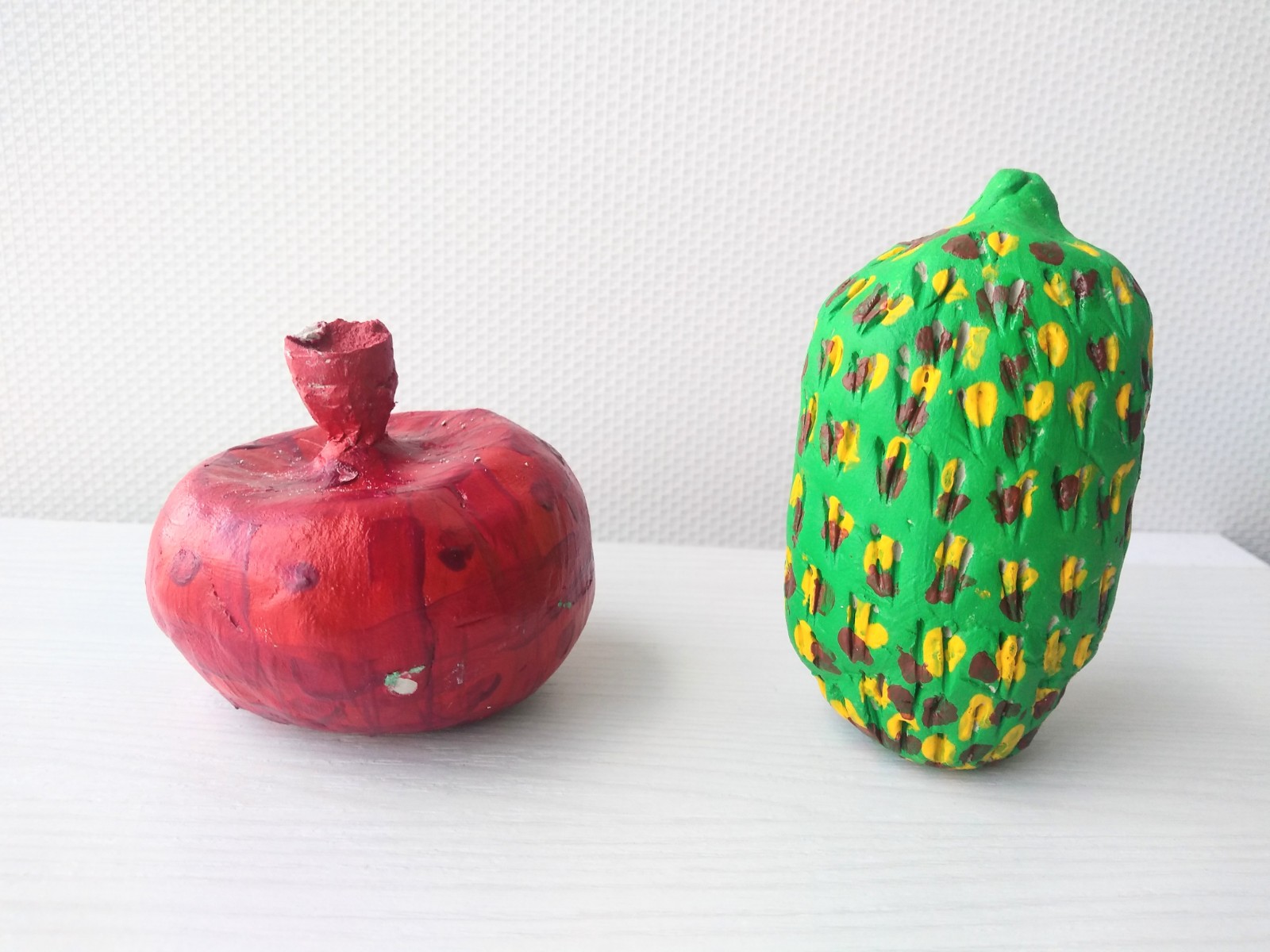 Two pieces of fruit, one red pomegranate and oval green fruit with yellow and brown spots.