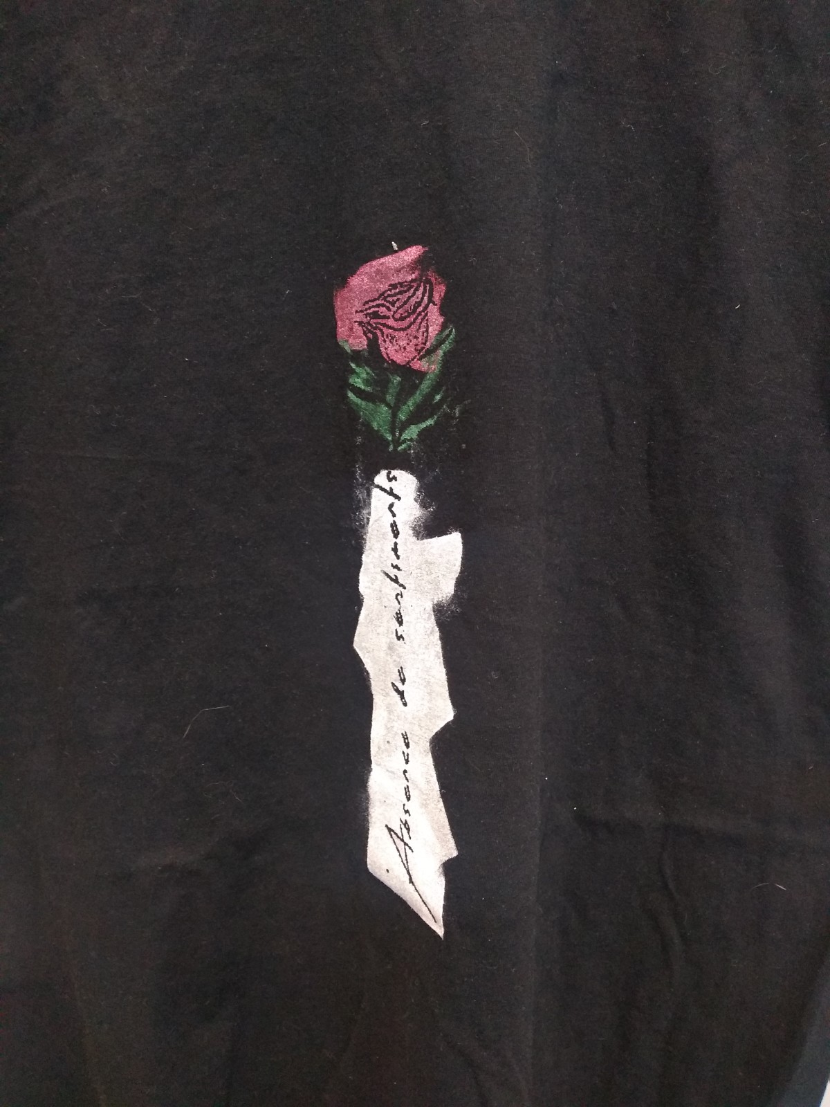 Red rose with green stem and text vertical reads Absence de sentiment with a brain attached to anatomical heart on black shirt.