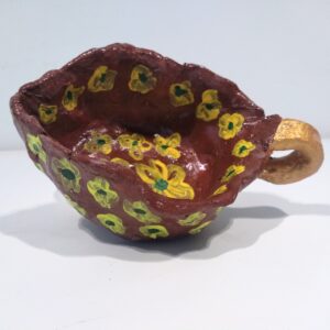 Maroon clay pot with yellow flowers and gold handle.