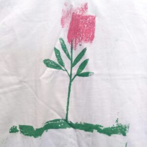 Red rose with green stem and leaves on a green coloured ground on white shirt.
