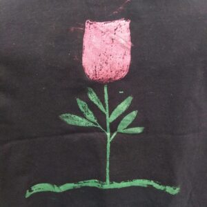 Red rose with green stem and leaves on a green coloured ground. Back of black shirt has a black and white skull.