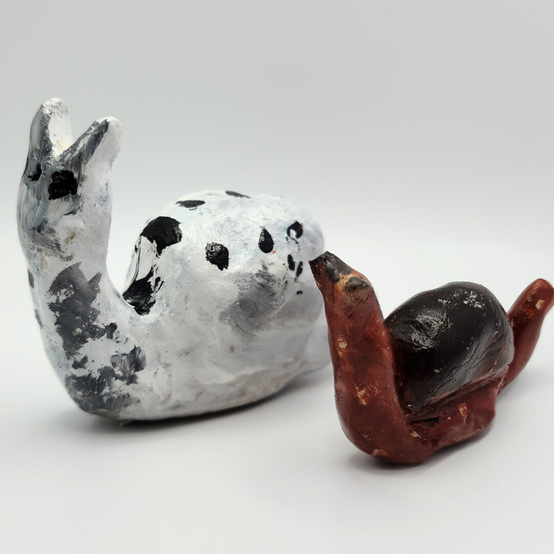 Sculpture of two snails, a larger one in white with black dots and a smaller one painted brown and black.