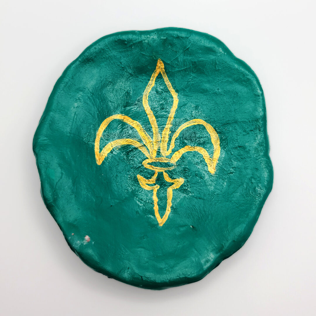 Top view of a clay green plate with a gold fleur-de-lis in the center.