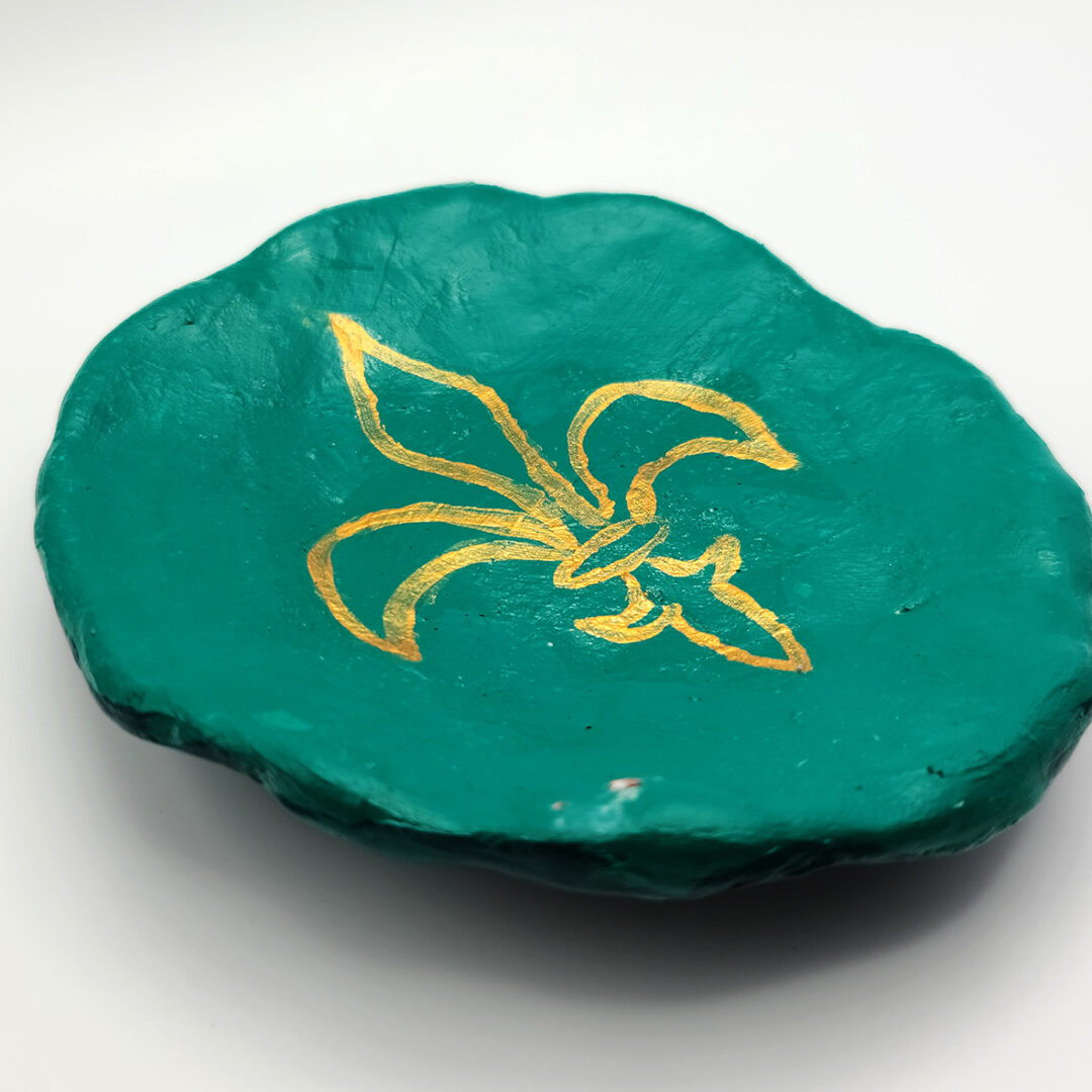 Clay green plate with a gold fleur-de-lis in the center.