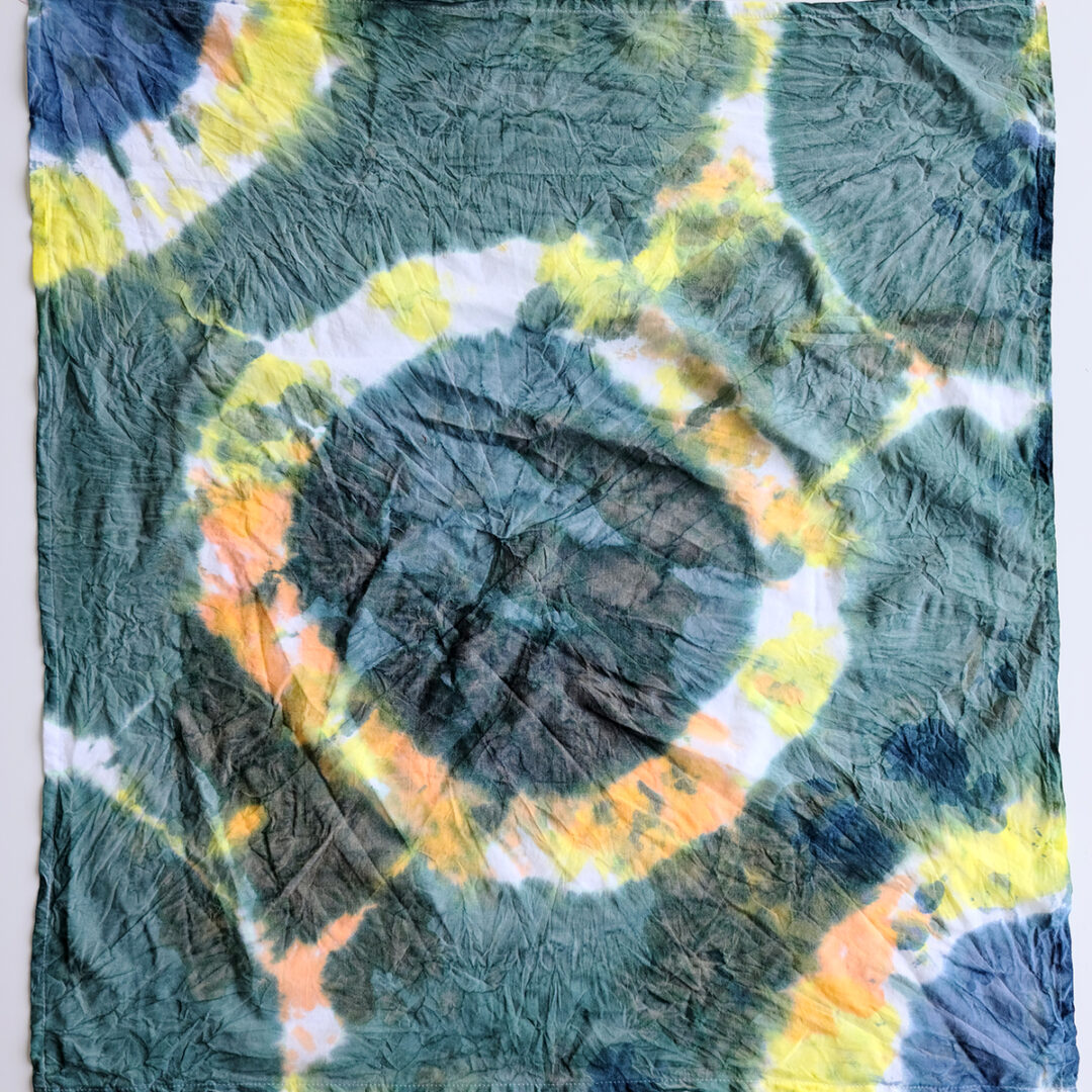 Tie dyed piece of fabric with dark green circles surrounded by yellow and blue.