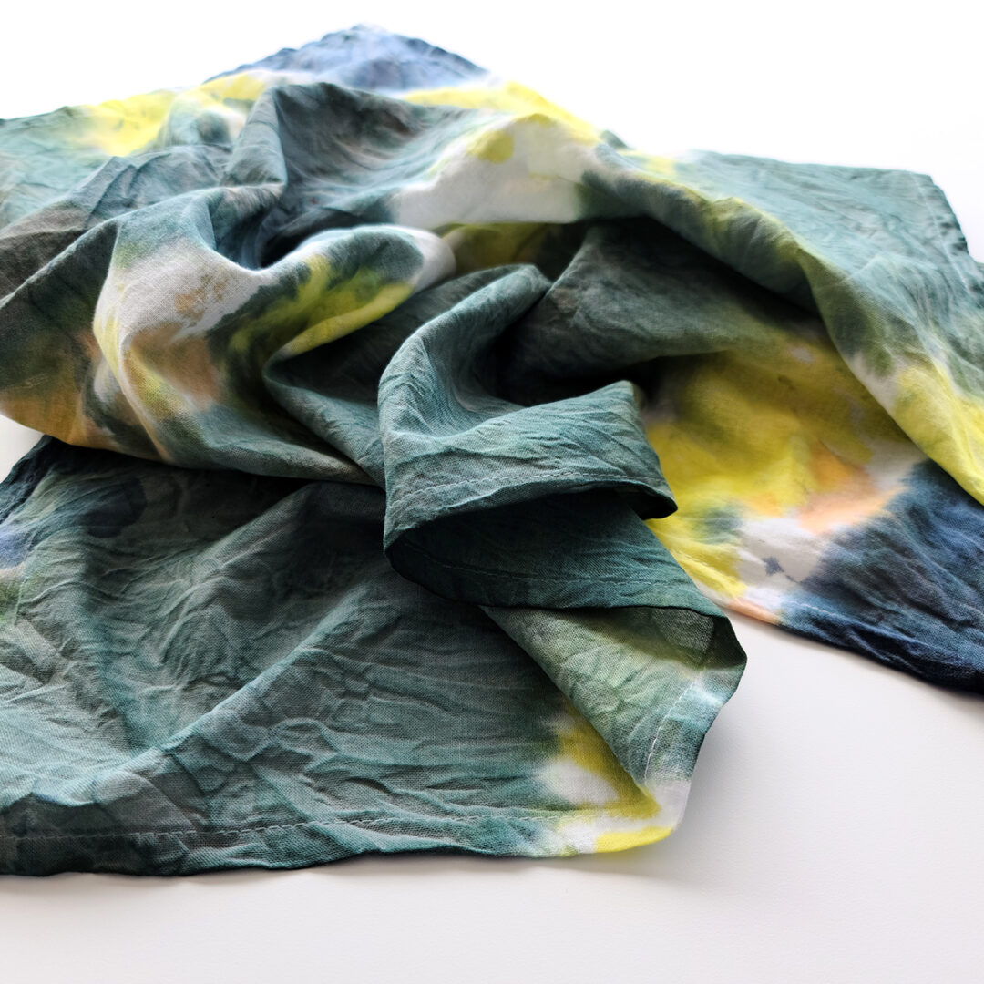 Crumpled close up of a tie dyed piece of fabric with dark green, yellow, and blue.