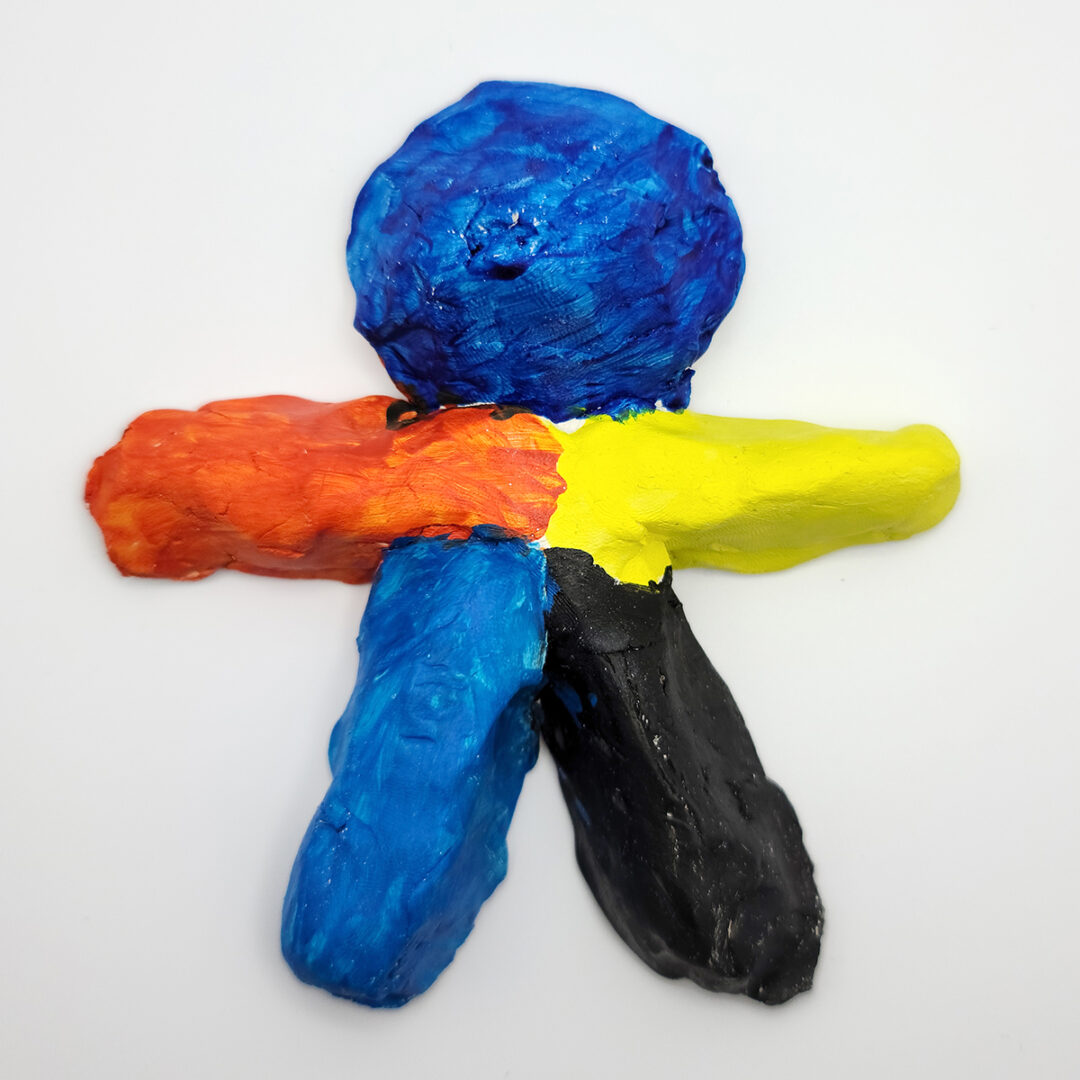 Clay sculpture of human figure with blue head, orange right arm, yellow left arm, blue right leg and black left leg.