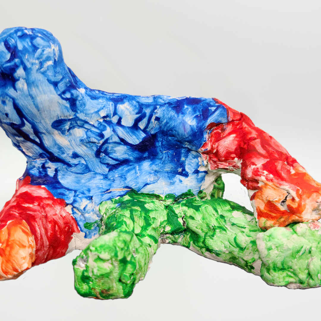 Clay sculpture of an abstracted reclining human figure with a blue head and torso, red and orange arms, and green legs.