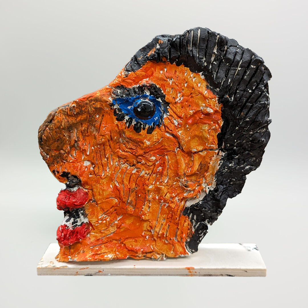 Clay sculpture of a side profile in orange with black hair and blue eyes.