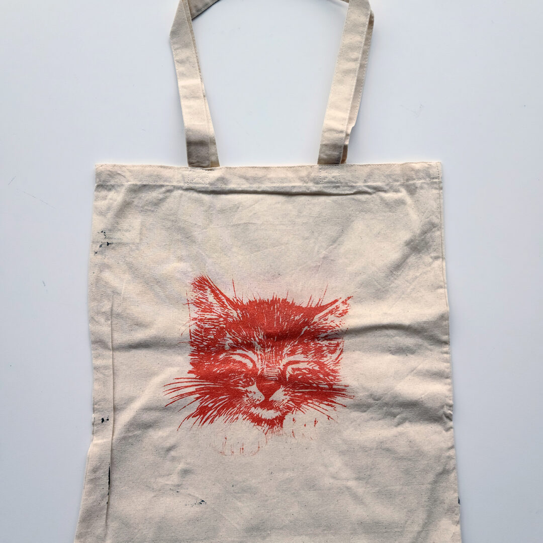 Tote bag with a screenprinted cat on it in red.